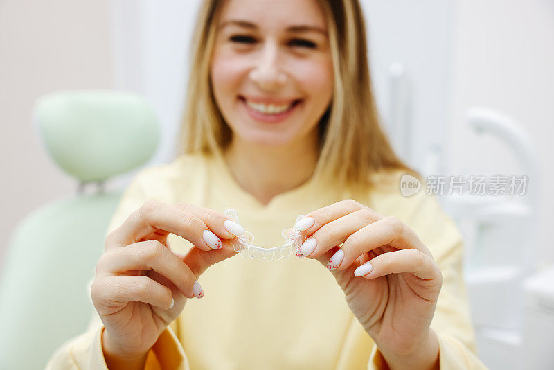 牙科隐形牙套或硅胶训练器在一个年轻的微笑女子的手中。正畸概念- Invisalign